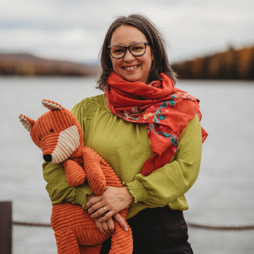 Photo d'Isabelle Charbonneau près d'un lac avec une peluche en renard dans les bras