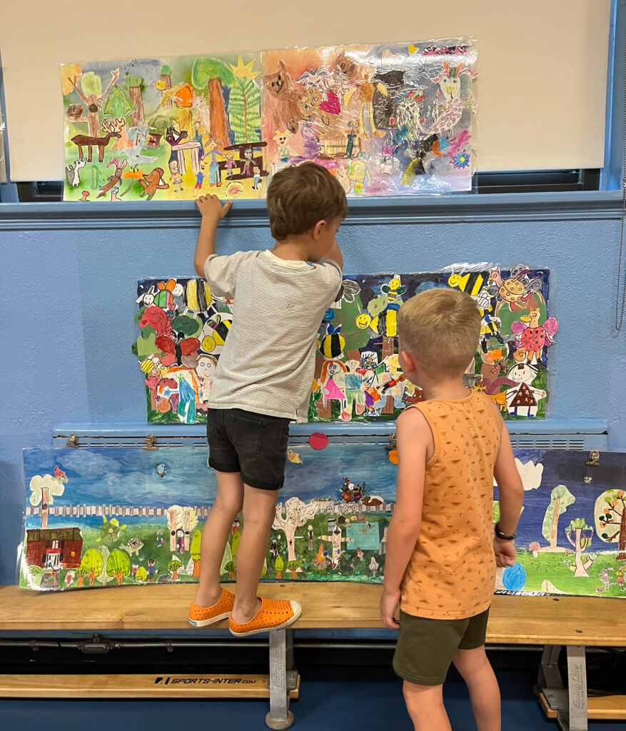 Deux jeunes garçons qui se tiennent debout devant des fresques composées de dessins d'enfants.