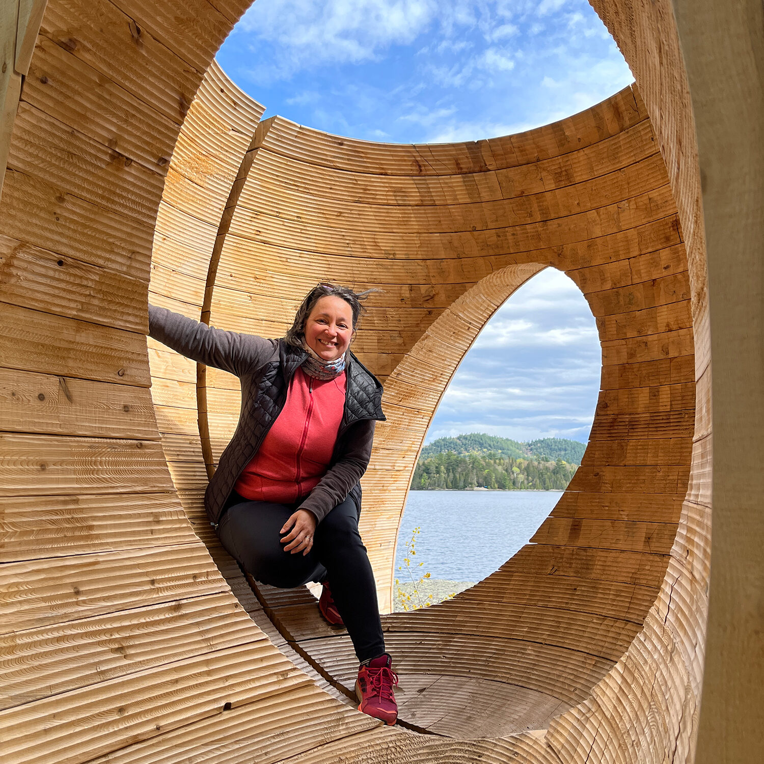 Isabelle Charbonneau souriante debout dans une grande sculpture en bois sculpté, à l’extérieur.