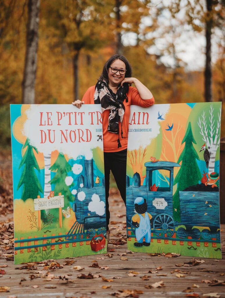 Isabelle Charbonneau devant un panneau de son illustration du p'tit train du Nord, en pleine forêt à l'automne.